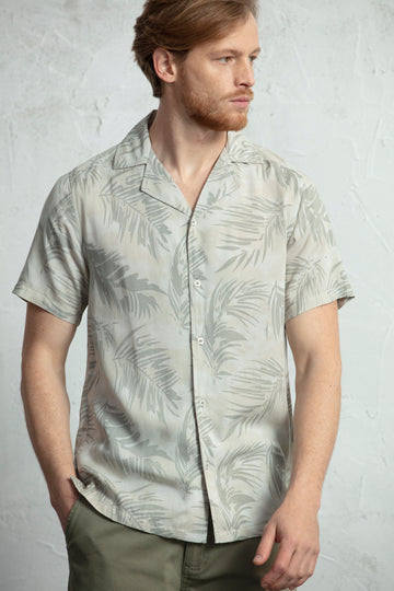 Camisa de manga curta estampada com folhas, decote de colarinho fecho com botões e confecionada em viscose.